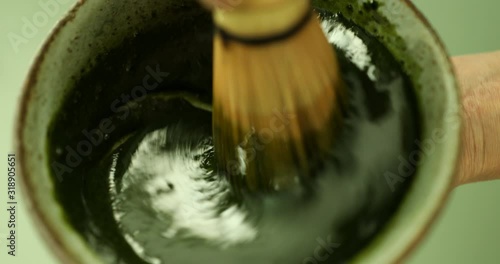 Blending green matcha tea powder in hot water with bamboo whisk to make green matcha tea latte