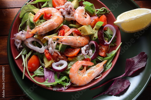 Sea food salad with shrimps, avocado, cherry tomatoes, red hot chilly pepper, red onion, arugula, beet leaves,rukola.balsamic sauce in a plate on a wood background Healthy sea food concept