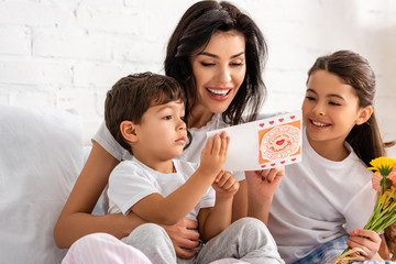 happy woman reading mothers day card while sitting in bed with adorable children