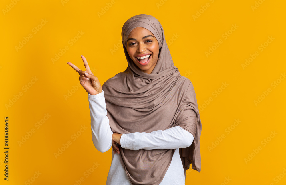 Joyful black muslim girl in headscarf showing peace gesture Joyful black muslim girl in headscarf showing peace gesture