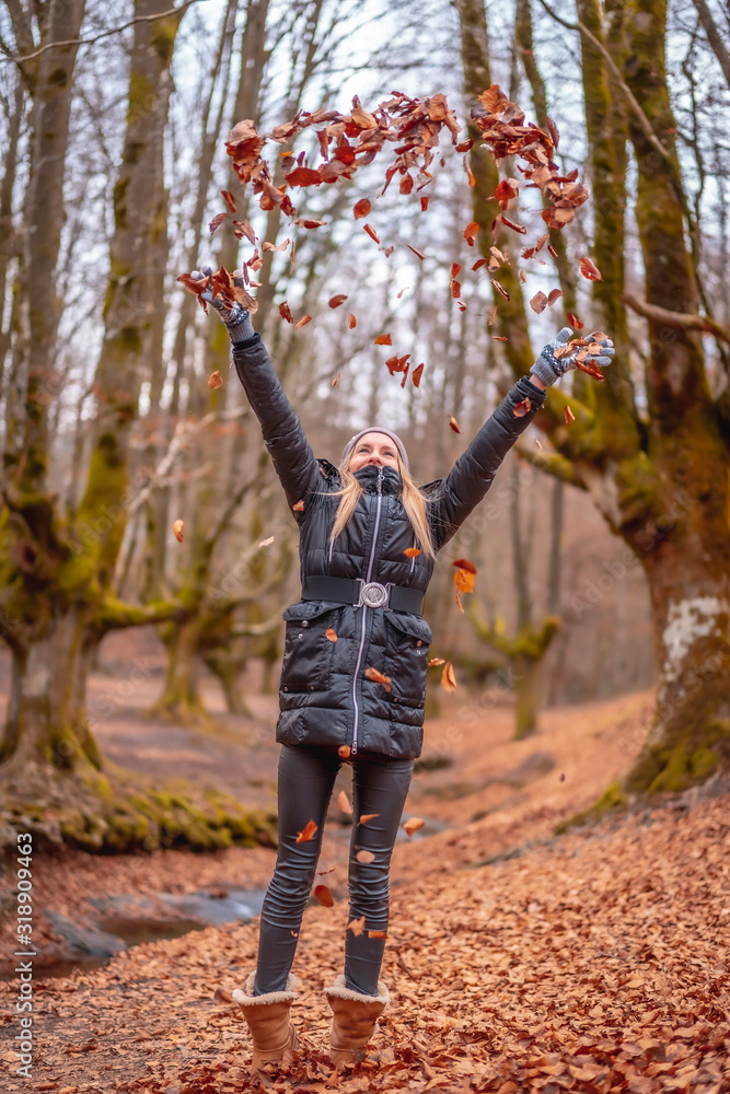 Fototapeta premium Blonde girl throwing leaves in a beautiful forest in winter