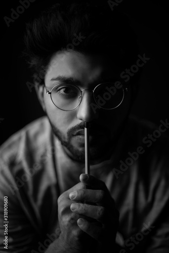 Monochrome fashion portrait of young Indian Bengali brunette man with traditional cotton wear and glasses holding pencil in black copy space background. Indian lifestyle and fashion photograph