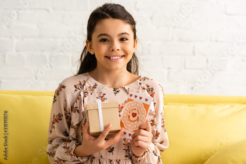 cute, happy child in elegant dress holding gift box and mothers day card with i love you mommy inscription photo