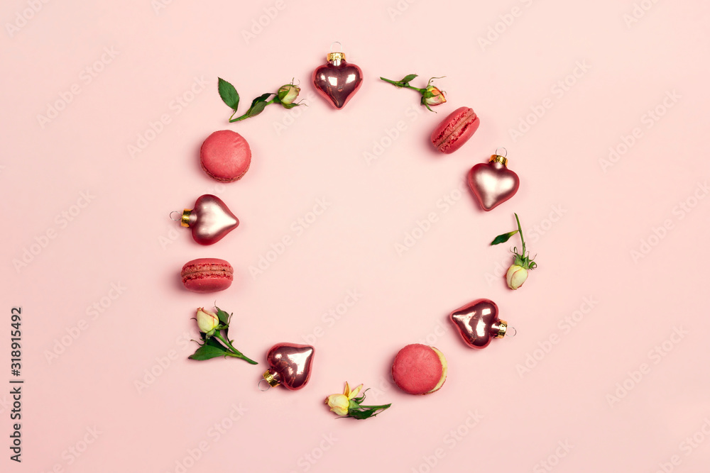 Round frame made of rose flowers, macarons and decorative hearts on pink background. St. Valentines day concept.