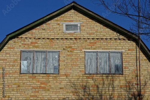 two large windows on an old brown brick attic of a rural house against a blue sky © butus