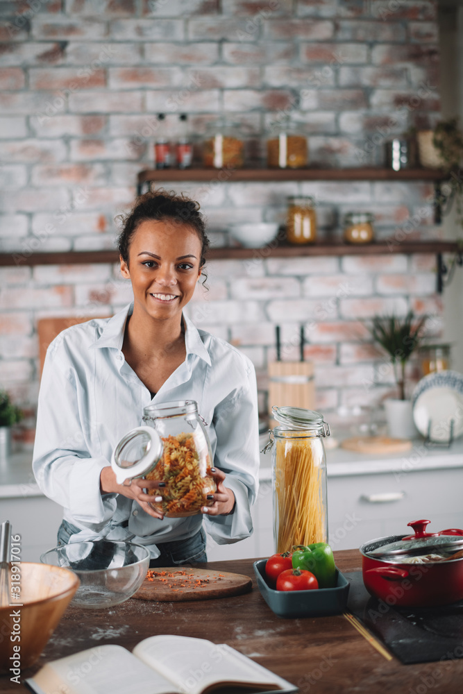 Young mixed race woman in kitchen. Beautiful woman cooking pasta. 