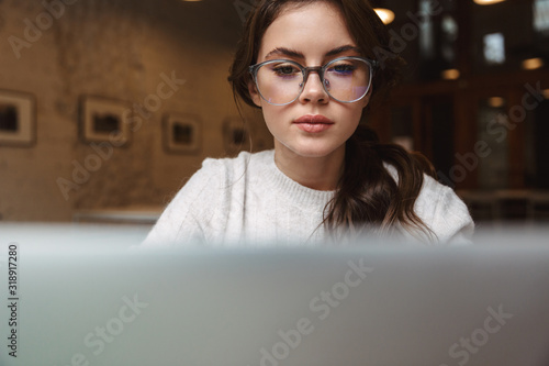 Εκτύπωση καμβά Image of young woman wearing eyeglasses using silver laptop in cafe