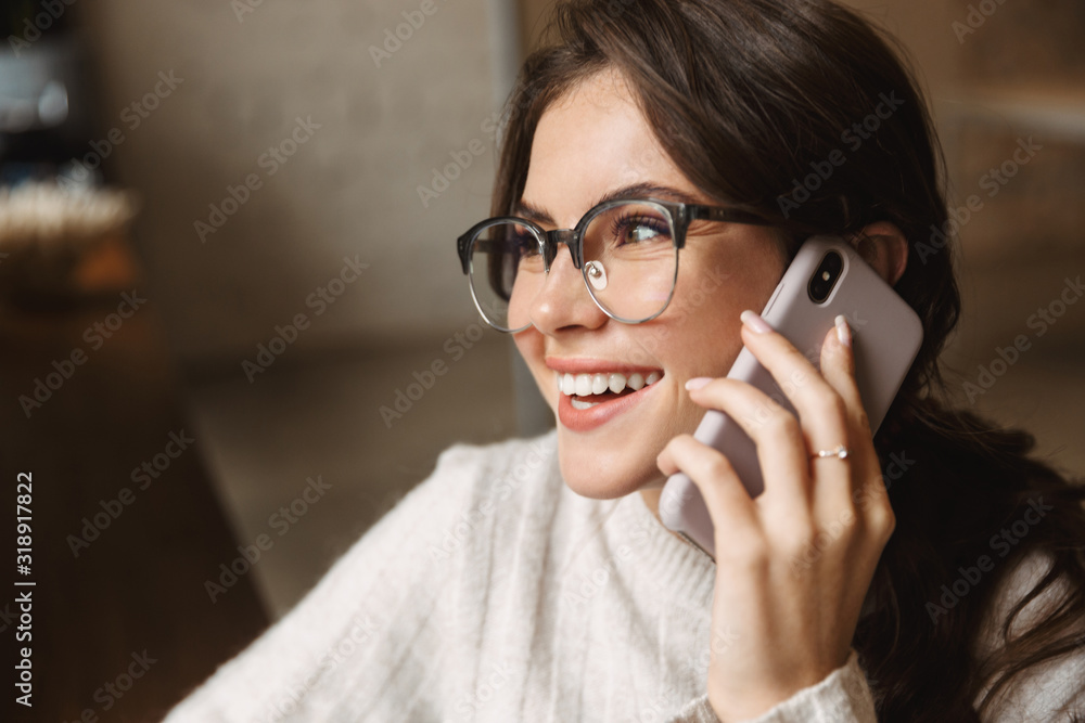 Image of young woman wearing eyeglasses talking on smartphone in cafe Image of young woman wearing eyeglasses talking on smartphone in cafe