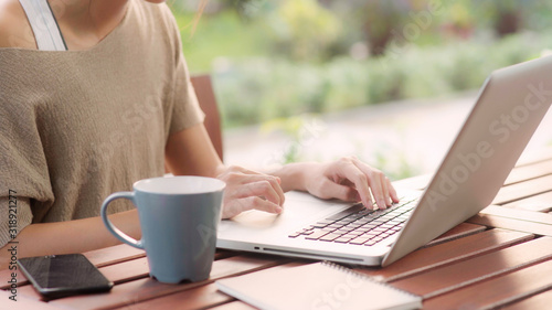 Freelance Asian woman working at home, business female working on laptop sitting on table in the garden in morning. Lifestyle women working at home concept.