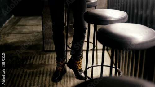 Young woman legs wearing black leather boots walking in the restaurant near bar chairs. Leather woman boots in the restaurant interiror.