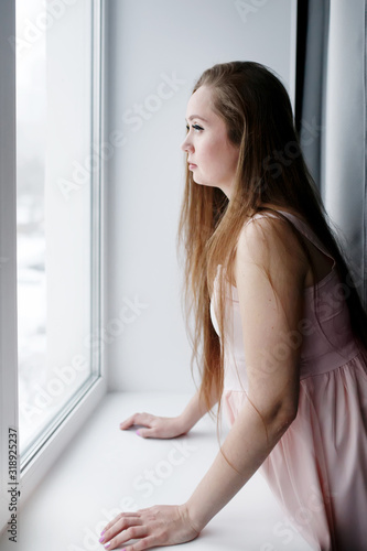 Young woman with long hair standing near window and looking out