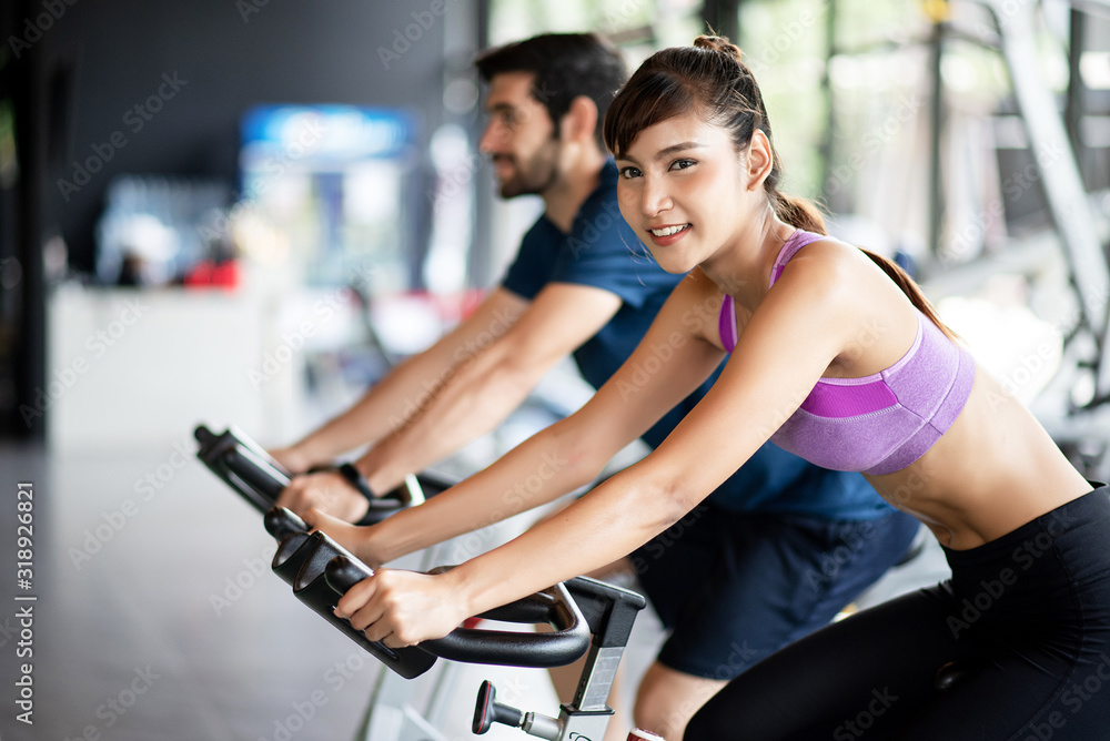 Asian healthy beautiful young woman bike cardio in the gym with her friends.