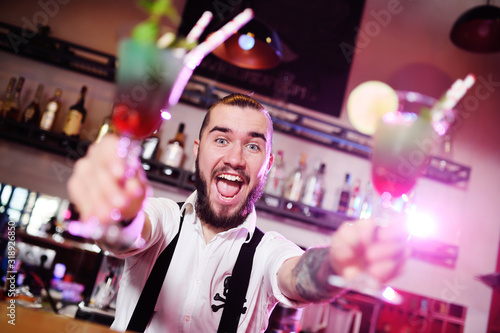 bartender smiling holding two glasses with colored cocktails on the background of the bar