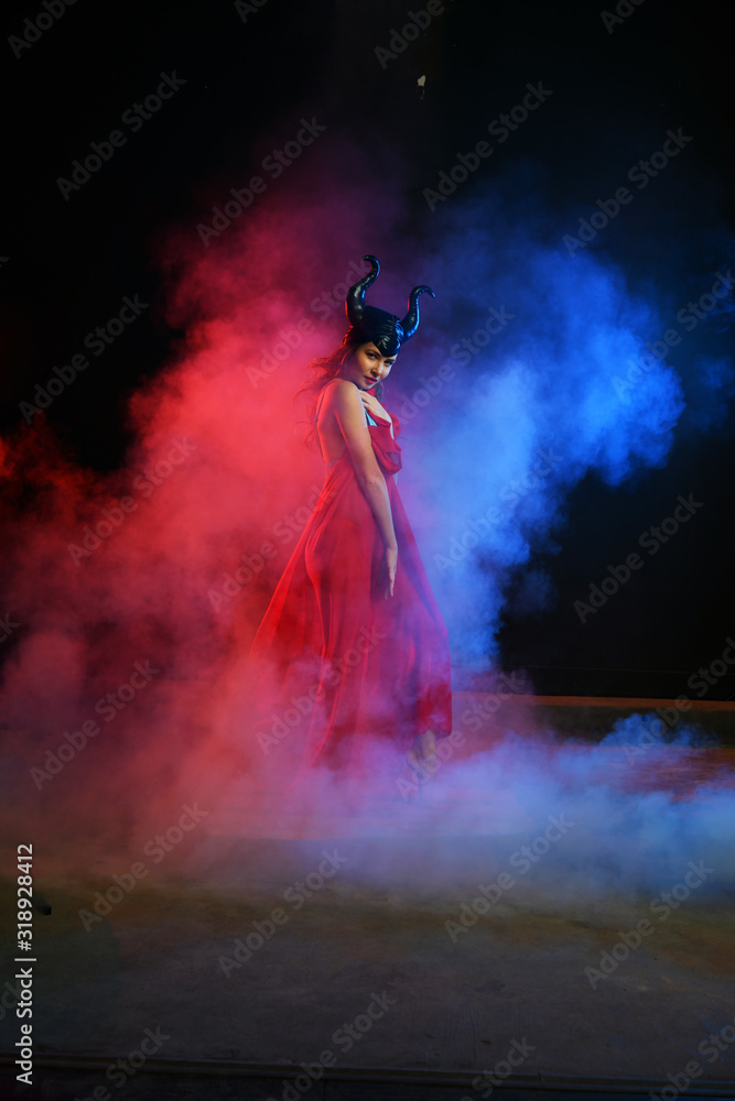 beautiful girl in a black helmet with horns on a blue-red background in smoke