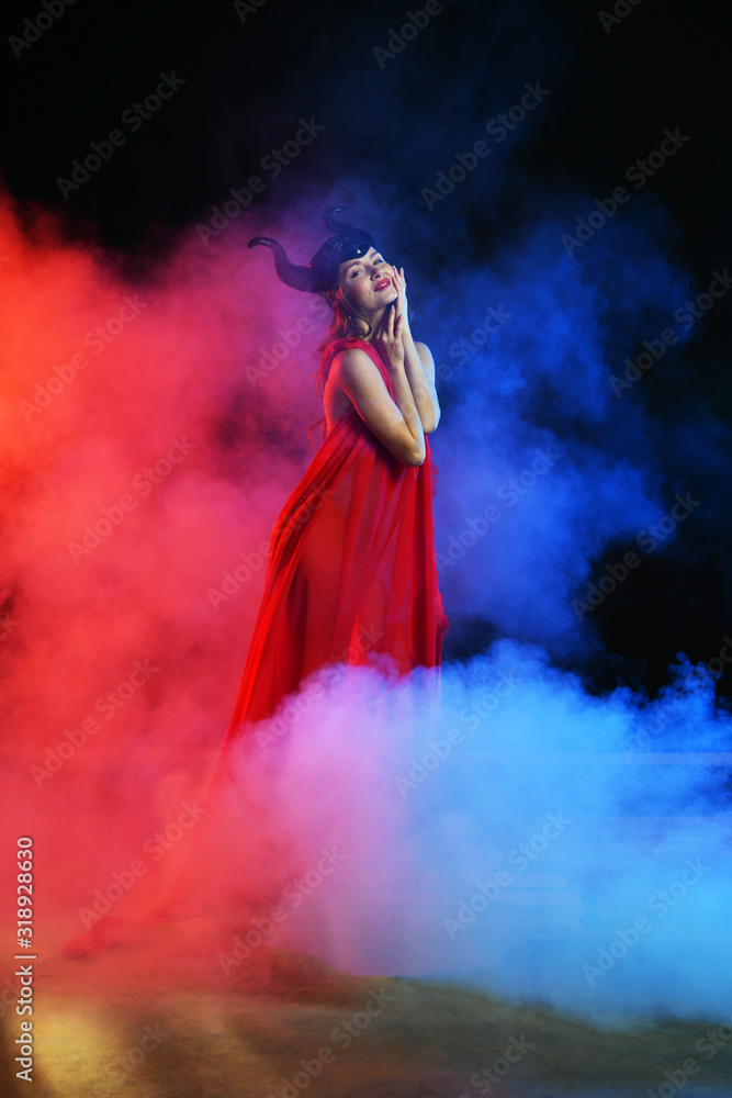 beautiful girl in a black helmet with horns on a blue-red background in smoke