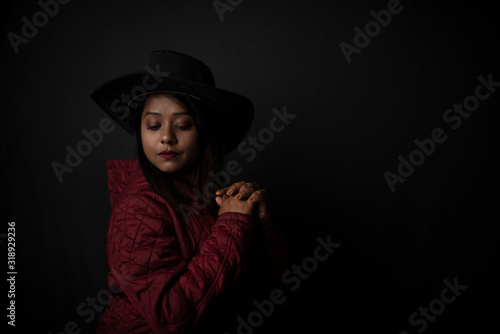 Fashion portrait of an young Indian Bengali brunette woman with maroon winter jacket and cowboy hat in black copy space background. Indian lifestyle and fashion photography. © abir