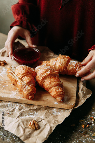 The girl is preparing dessert. Croissants with raspberry jam. Fresh pastries on a wooden background.