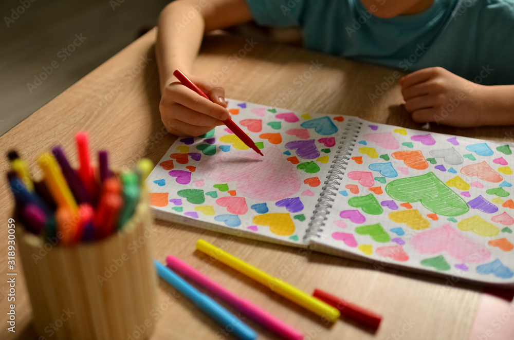 Child's hands draw hearts of different colors in a notebook. Close-up photo. Child's hands draw hearts of different colors in a notebook. Close-up photo.
