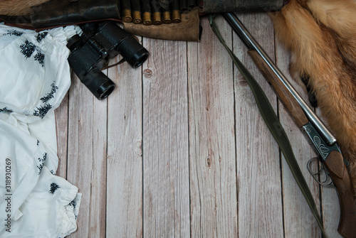 Hunting equipment. Hunting weapons, white camouflage suit, bandolier with cartridges, Fox skin, binoculars on a light wooden background. Free space. photo