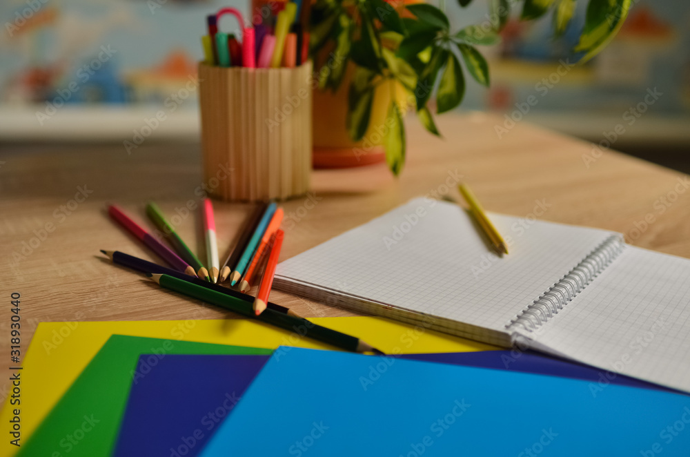 Notebook and color pencils on a desk. A cozy corner in the house. Notebook and color pencils on a desk. A cozy corner in the house.
