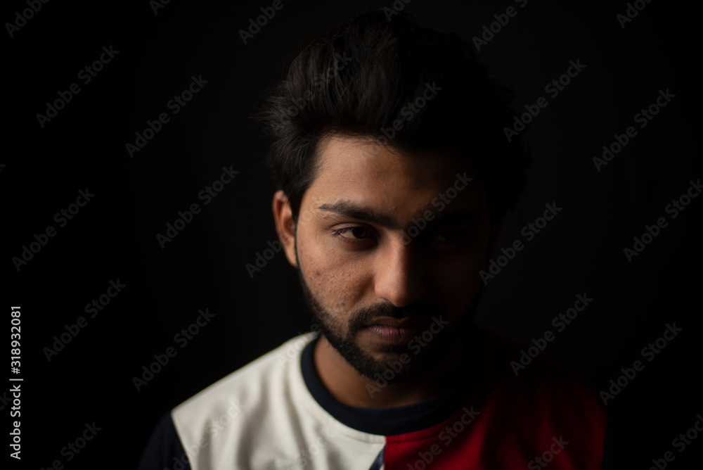 Fashion portrait of young and handsome Indian Bengali brunette man with casual tee shirt showing facial expression in black copy space background. Indian lifestyle and fashion photography