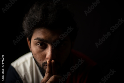 Fashion portrait of young and handsome Indian Bengali brunette man with casual tee shirt showing facial expression in black copy space background. Indian lifestyle and fashion photography