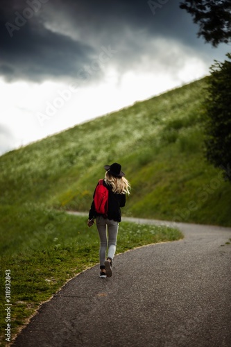 Young caucasian backpacker female in hat walking on a countryside asphalt road near the green meadow.Outdoor,Traveler concept.