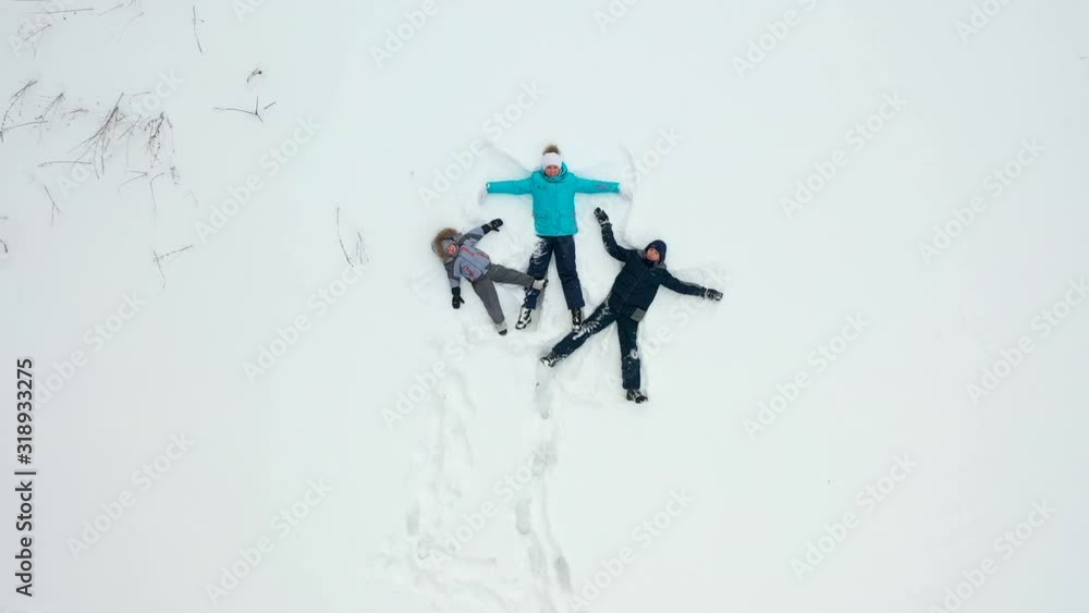 A family with children makes a figure of a snow angel in a clearing in the forest. Aerial photography of a girl and children lying in the snow. A family with children makes a figure of a snow angel in a clearing in the forest. Aerial photography of a girl and children lying in the snow.