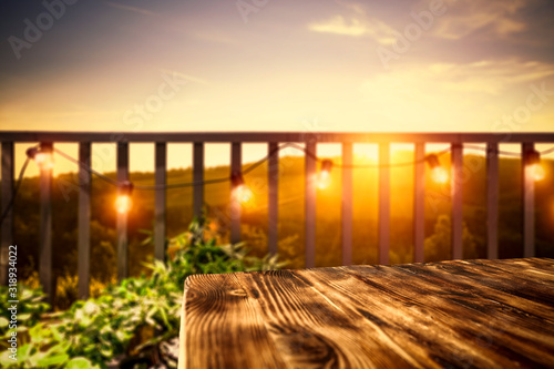 Wooden board of free space for your decoration. Blurred background of balcony and ladnscape of Tuscany.Small lights and orange color of sunset time.  © magdal3na