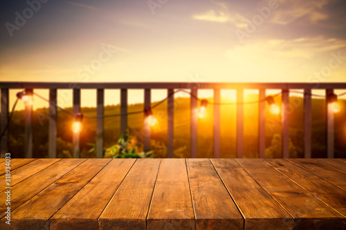 Fototapeta Naklejka Na Ścianę i Meble -  Wooden board of free space for your decoration. Blurred background of balcony and ladnscape of Tuscany.Small lights and orange color of sunset time. 