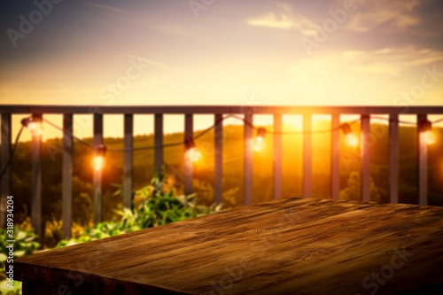 Wooden board of free space for your decoration. Blurred background of balcony and ladnscape of Tuscany.Small lights and orange color of sunset time. 