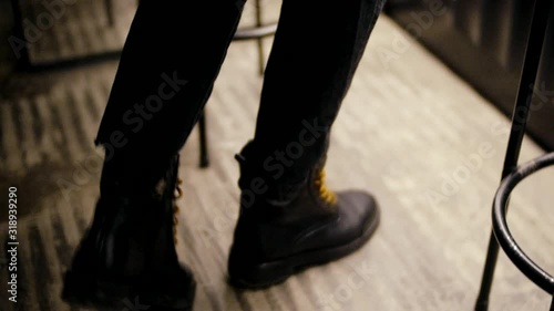 Young woman legs wearing black leather boots walking in the restaurant near bar chairs. Leather woman boots in the restaurant interiror.
