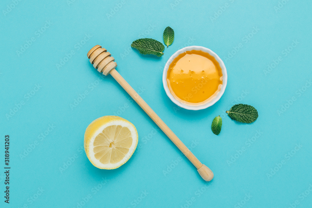Honey bowl with honey deeper, lemon and mint on a blue background Honey bowl with honey deeper, lemon and mint on a blue background