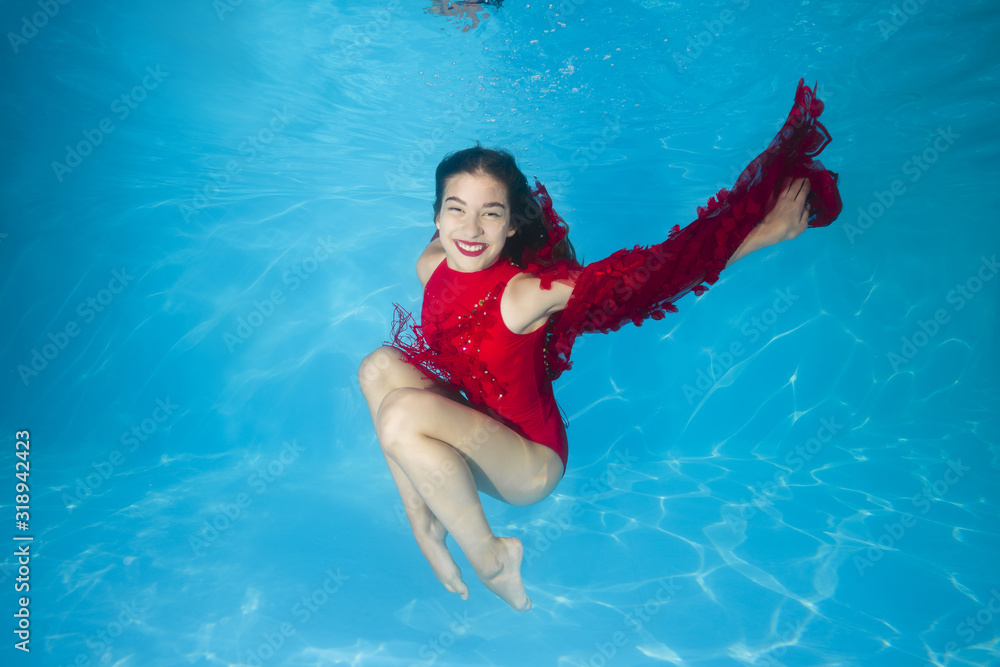 Young beautiful girl in a red dress posing underwater in the pool