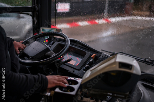 The drivers cab of the public bus, his hand on the drivers wheel, outside the window - it s rainy. Close-up.