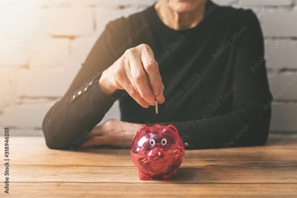 retirement savings - senior woman putting coin into a piggy bank retirement savings - senior woman putting coin into a piggy bank