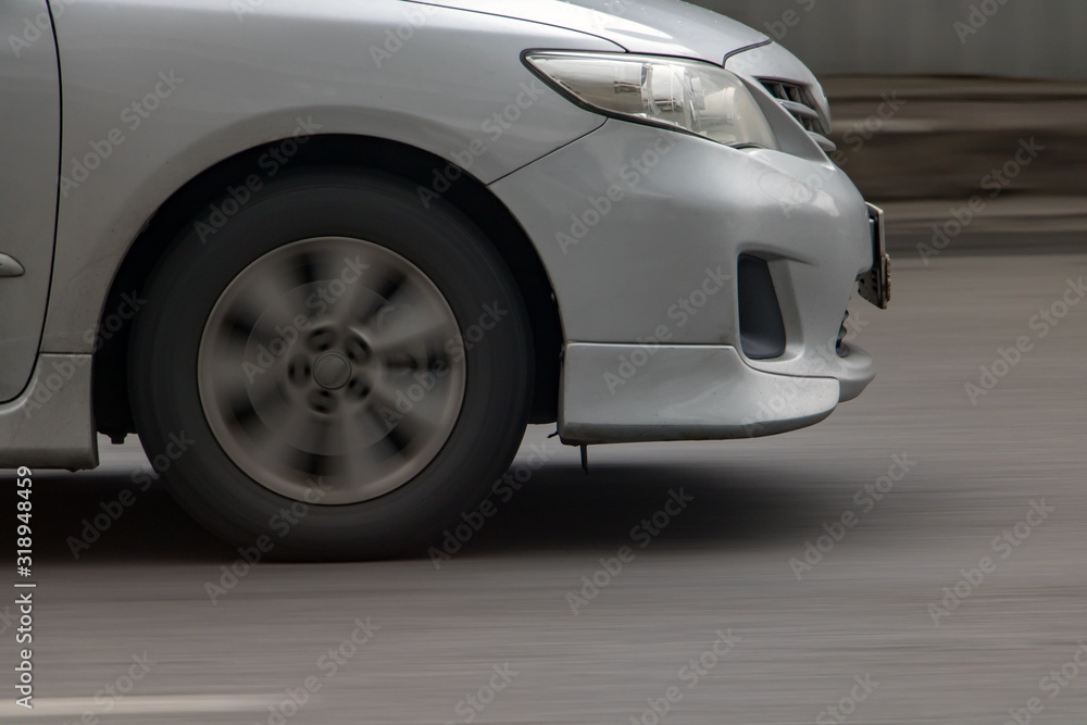 Detail of front of car driving on asphalt. Car front wheel rotates on road, motion blurred background. Detail of front of car driving on asphalt. Car front wheel rotates on road, motion blurred background.