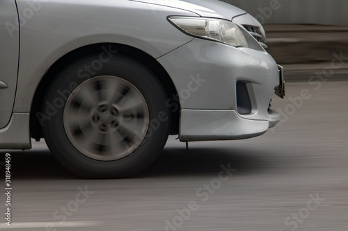 Detail of front of car driving on asphalt. Car front wheel rotates on road, motion blurred background.