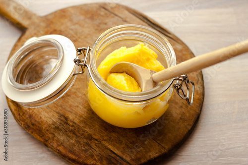 Ghee clarified butter desi in glass jar with spoon made from wood on natural wooden background photo