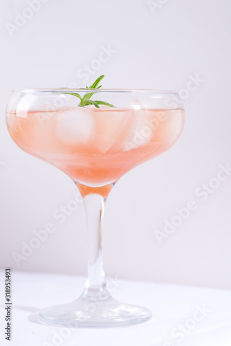 Pink cocktail with rosemary and ice on a white tablecloth on the table