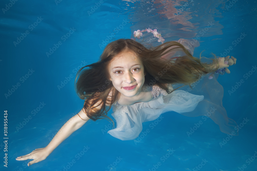 Young beautiful girl in a white dress posing underwater in the pool