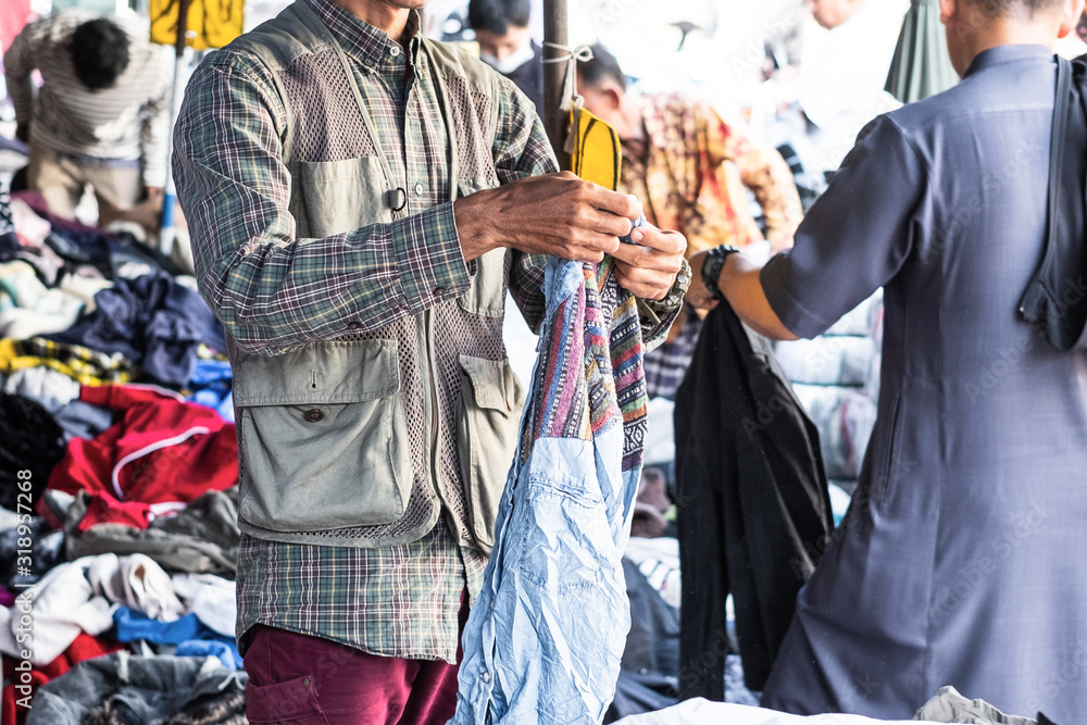 Thai man is choosing used second hand clothes at flea market in Thailand