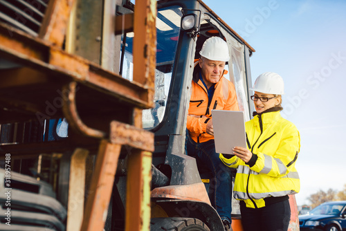 Worker in forklift and forewomen looking into task list