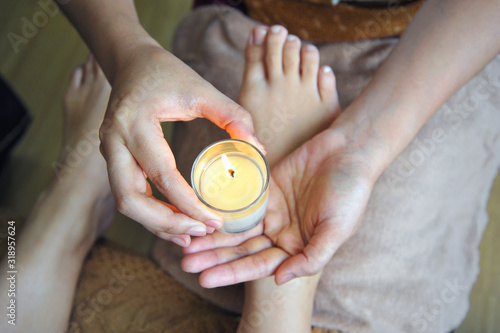 Closeup of masseuse hands pouring wax from a candle, foot massage in spa salon.
