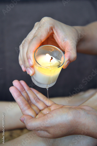 Closeup of masseuse hands pouring wax from a candle, foot massage in spa salon.