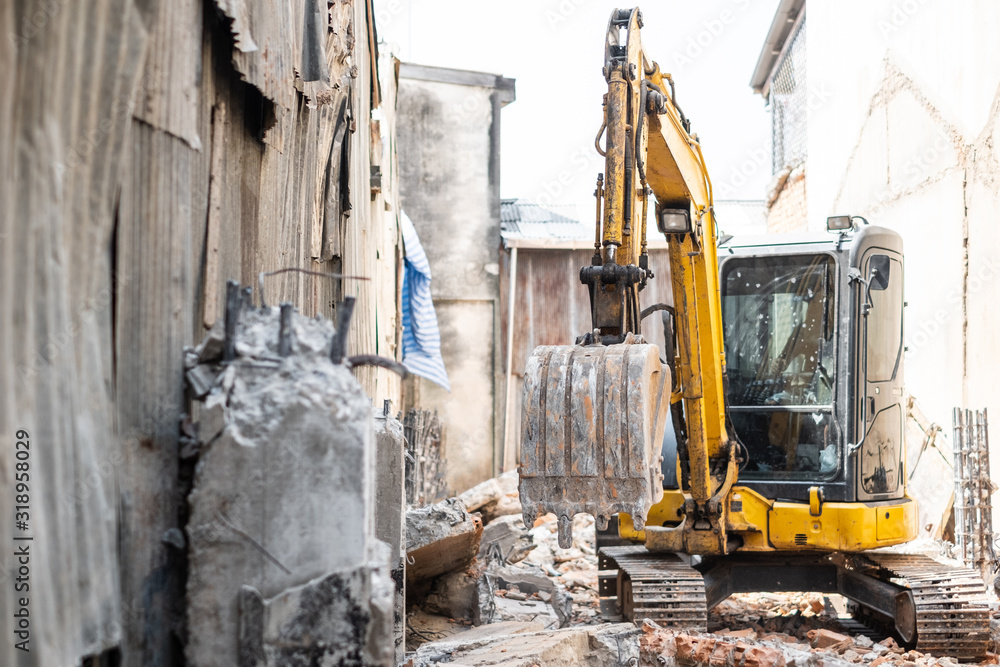 Small yellow excavator is on duty for pulling down the old buildings. Selective focus at bucket. Small yellow excavator is on duty for pulling down the old buildings. Selective focus at bucket.