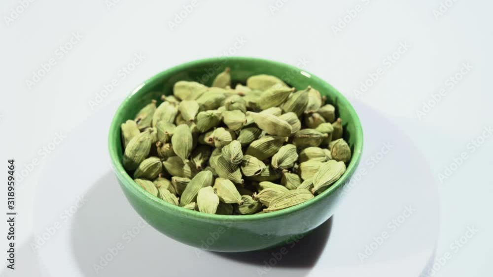 Rotation of green dried aromatic cardamom pods in small green bowl Rotation of green dried aromatic cardamom pods in small green bowl