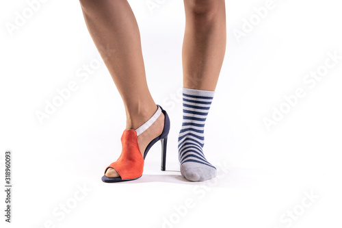 Feet of woman on white background.One foot wears an elegant red and blue heel shoe and the other foot is without a shoe only with a gray and blue striped sock.