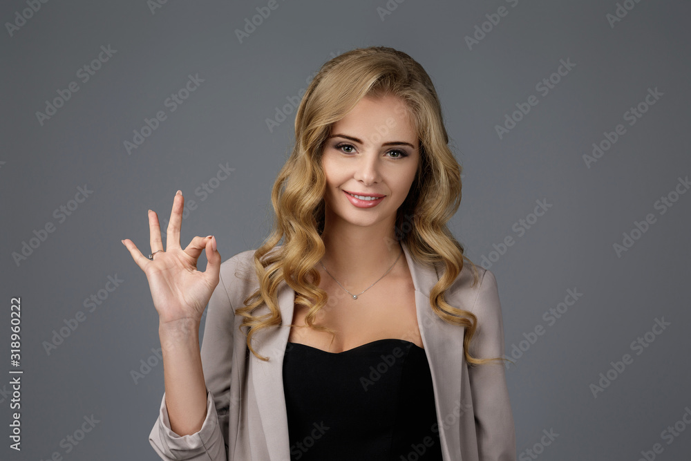 smiling young curly woman showing OK gesture on gray background. smiling young curly woman showing OK gesture on gray background.