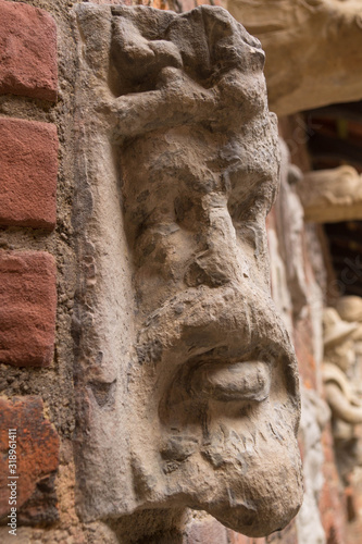 An old stone sculpture, gargoyle in the shape of a male face on a brick wall